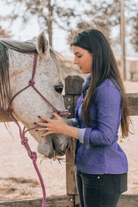 Side view of woman touching horse in barn