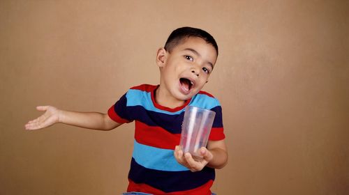 Portrait of boy holding drinking glass while gesturing against wall