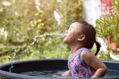 Close-up of girl spraying water with mouth while sitting in wading pool