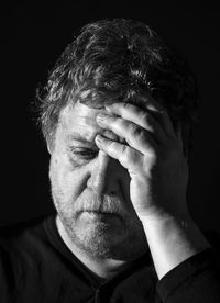 Close-up of sad mid adult man with head in hands against black background