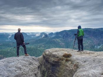 Rear view of men standing on rock against mountains
