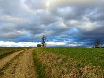 Dirt road amidst field against sky