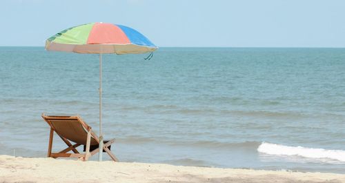 Deck chair and beach umbrella at beach against clear sky