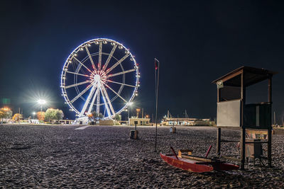 Illuminated ferris wheel at beach against sky at night