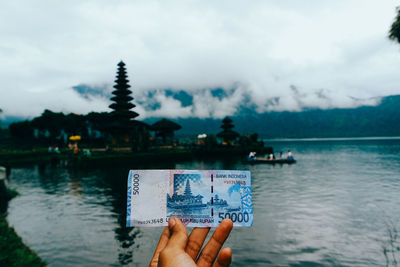 Cropped hand holding paper currency by river 