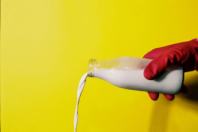 Close-up of hand pouring milk from bottle against yellow background