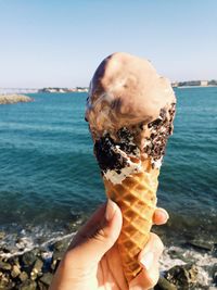 Close-up of hand holding ice cream cone at sea