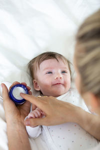 Cropped hand of woman holding cream by son on bed