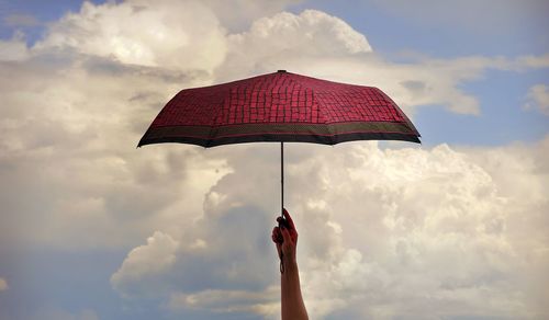 Low angle view of hand holding umbrella against sky