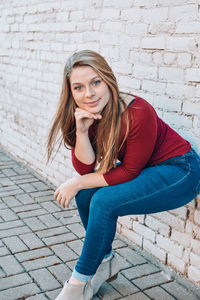 Portrait of young woman sitting against wall