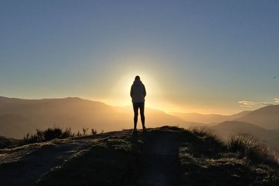 Rear view of silhouette person standing on mountain during sunset