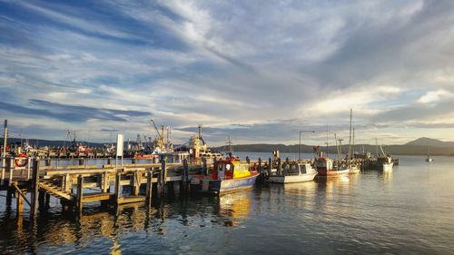 Boats moored at harbor against sky during sunset