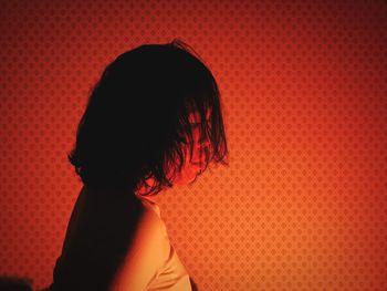 Side view of woman standing by wall in illuminated room