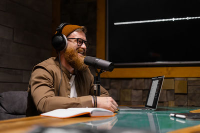 Smiling and gesturing radio host with headphones reading news into studio microphone