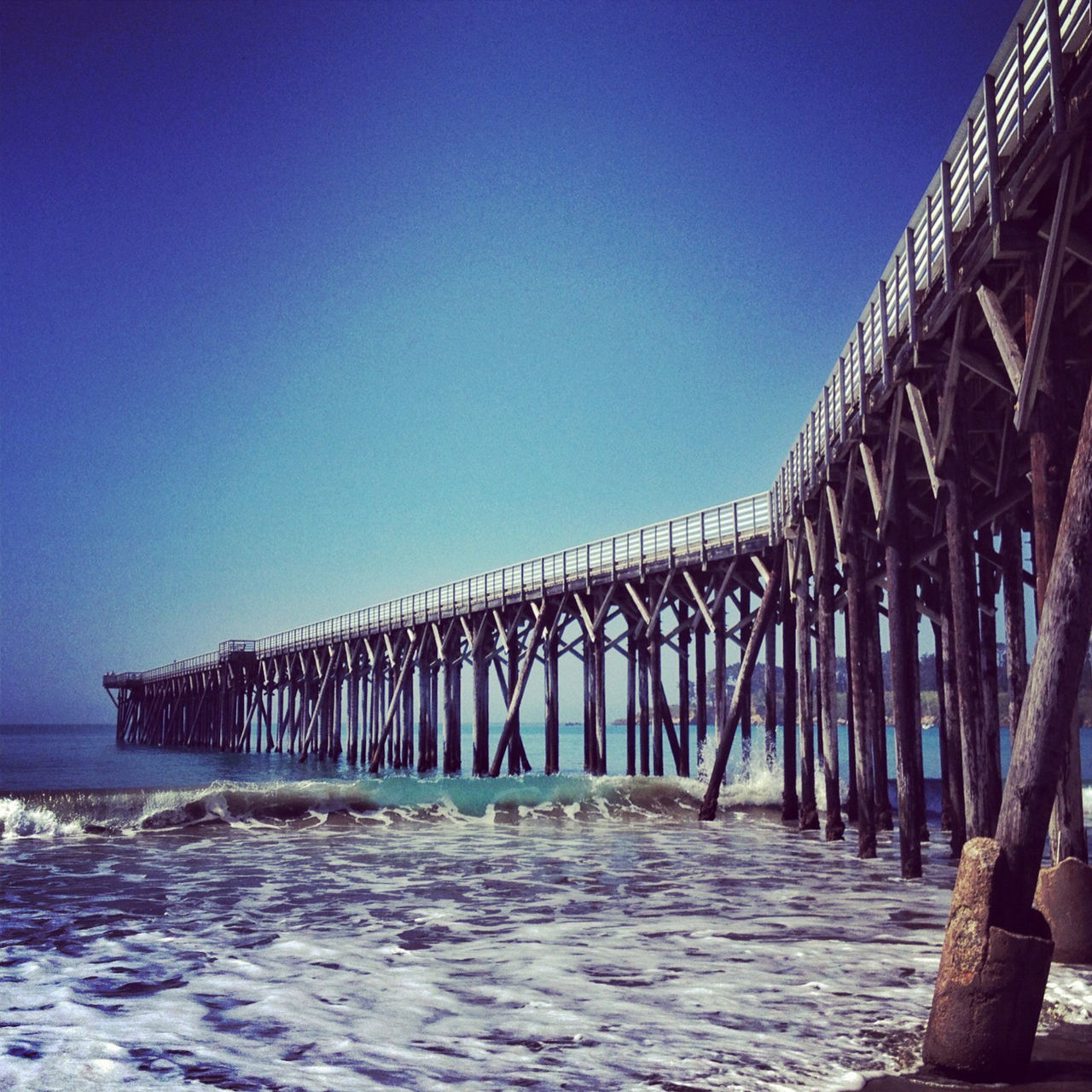 clear sky, sea, water, beach, built structure, blue, architecture, copy space, pier, tranquility, horizon over water, tranquil scene, nature, sand, sky, connection, bridge - man made structure, low angle view, scenics, shore