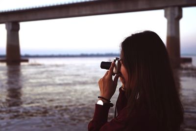 Side view of woman photographing sea through camera during sunset