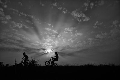 Silhouette people riding bicycle on field against sky during sunset