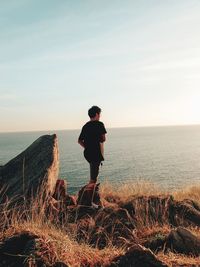 Rear view of man standing on beach against sky during sunset