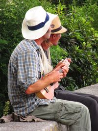 Midsection of man holding hat while sitting by plants