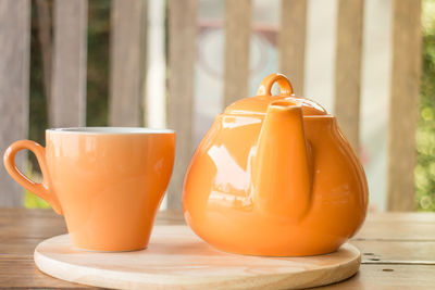 Close-up of orange cup and teapot on wooden table