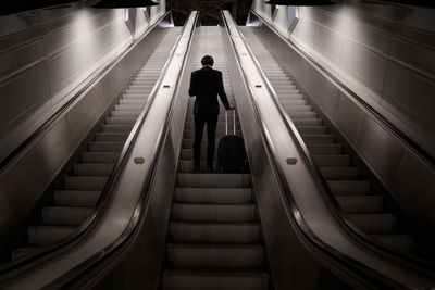 Low angle view of businessman standing with luggage on escalator in airport