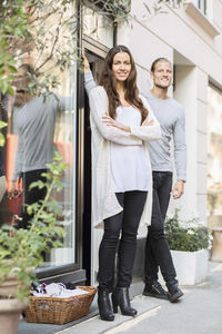 Portrait of smiling owner with female worker standing outside clothing store