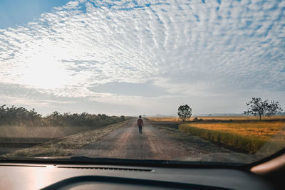 Rear view of boy walking on road seen through car windshield