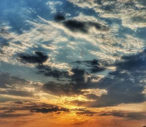 Low angle view of sunlight streaming through clouds during sunset