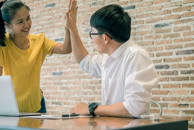 Business colleagues joining hands while sitting at table against brick wall