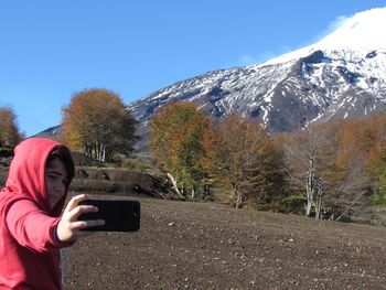 Boy taking selfie while standing on field by snowcapped mountain