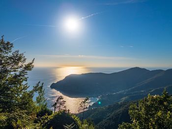 Scenic view of sea and mountains against bright sun