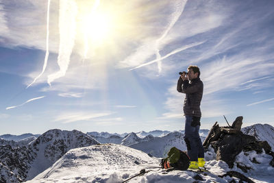 Man photographing on snow covered mountain against sky