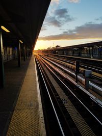 Railroad station platform against sky during sunset