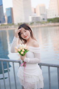 Portrait of smiling young woman standing against lake