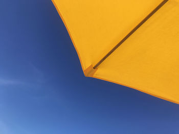 Low angle view of parasol against clear blue sky