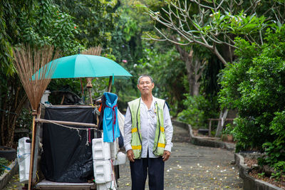 An old asian man street cleaner standing next to an old garbage cart before going to work