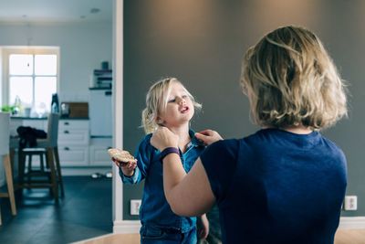 Rear view of mother dressing daughter at home