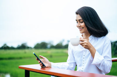 Young woman holding coffee cup on mobile phone