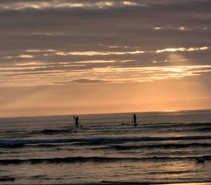 Silhouette people standing on beach against sky during sunset