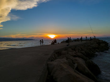 Silhouette people on beach against sky during sunset