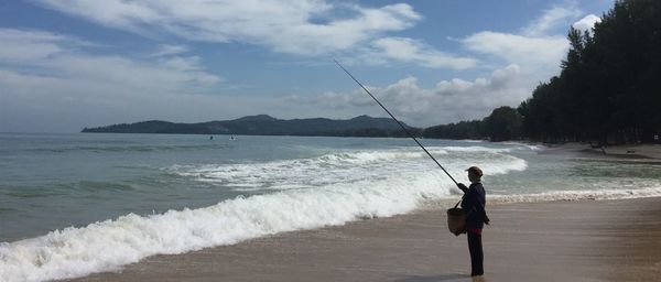 Man fishing at beach against sky