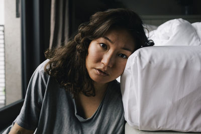 Portrait of tired lonely woman leaning on bed at home