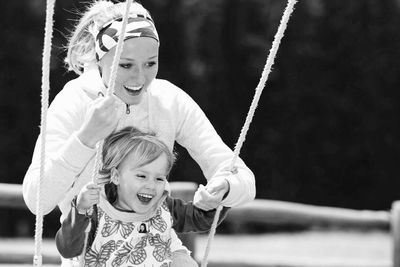 Happy mother pushing daughter on swing at playground