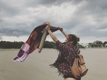 Woman holding umbrella at beach against sky