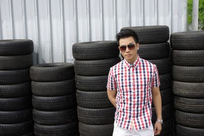 Portrait of man in sunglasses standing against tires