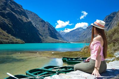 Woman sitting on mountain by sea against mountains