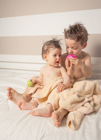 Cute shirtless siblings wrapped in towel against wall