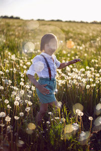 Funny happy child sit in hat on field with white dandelions  sunset in summer. soap bubbles  flying