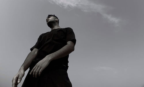 Low angle view of young man looking away against sky