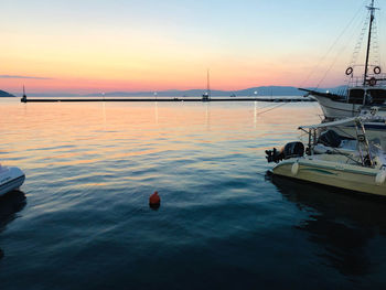 Sailboats moored on sea against sky during sunset